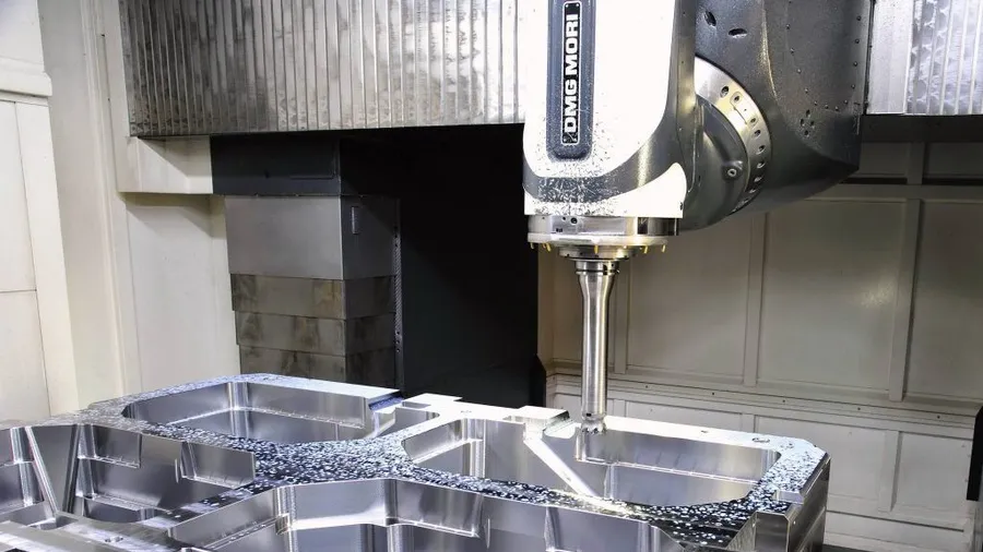 A five-axis machining centre cutting a large mold block, with the tool spindle positioned over the freshly machined cavity.