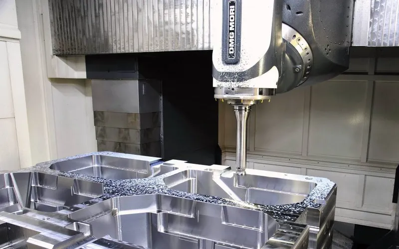 Tool spindle of a five-axis machining centre above a freshly cut cavity in a large steel mold block.