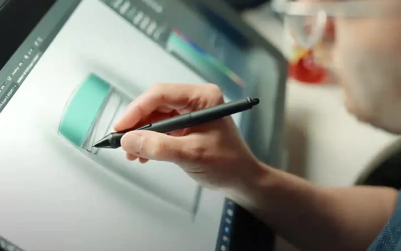A designer's hand holds a stylus over a pen display showing a container product sketch.