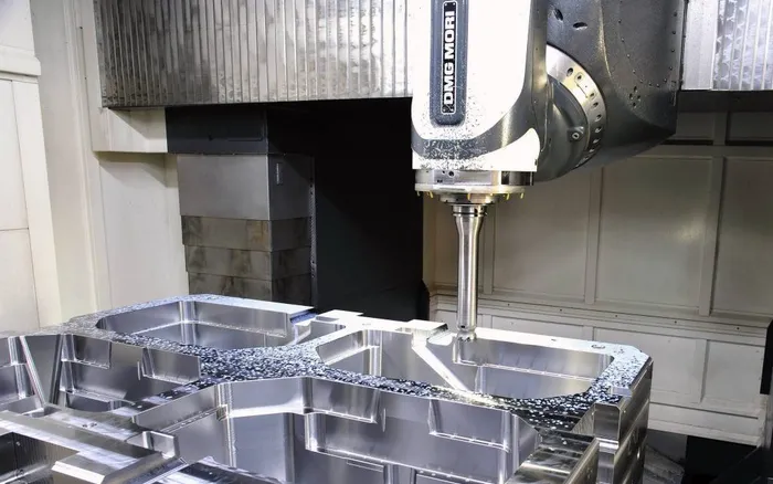 Tool spindle of a five-axis machining centre above a freshly cut cavity in a large steel mold block.