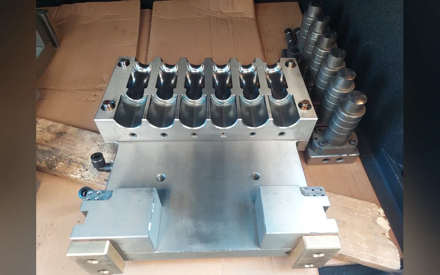 A six-cavity injection stretch blow mold with its preform cores beside it